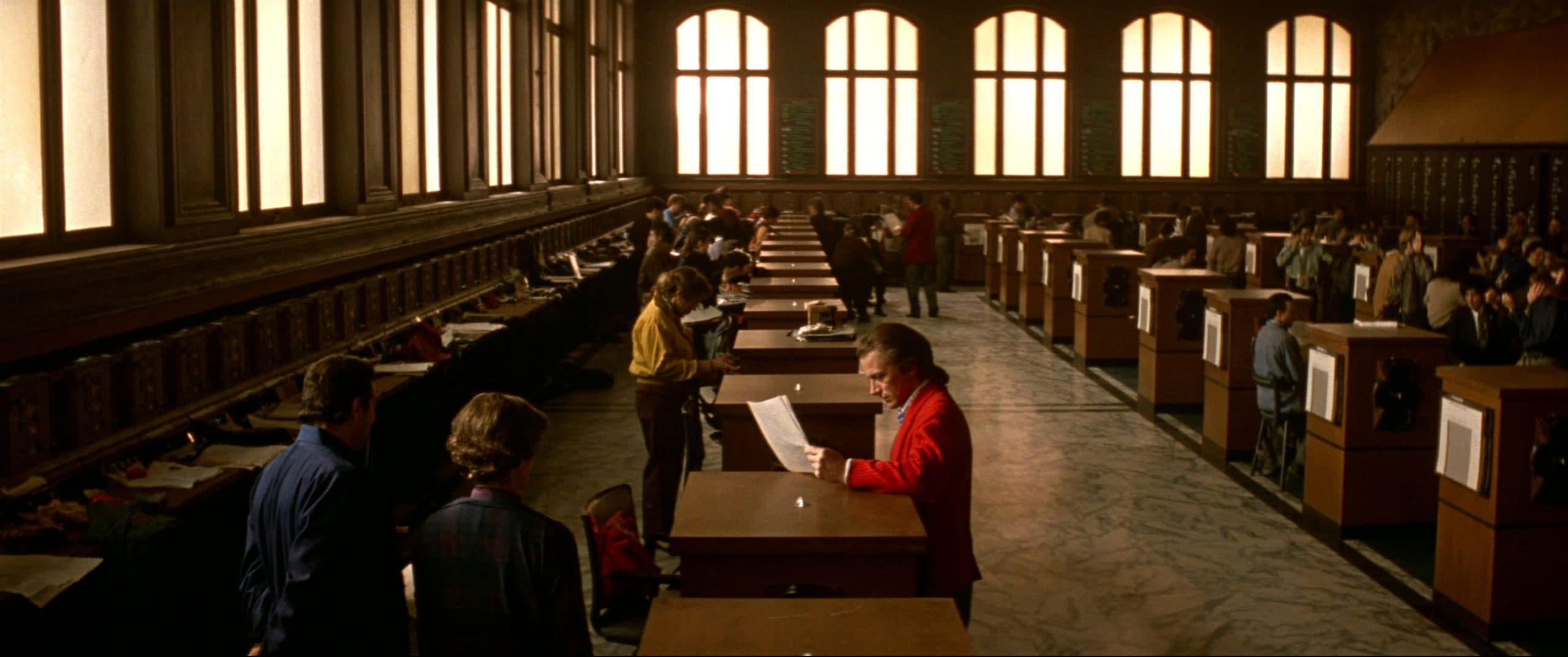 A quiet 1980s exchange trading floor in warm window light, traders in colored jackets reading at their posts